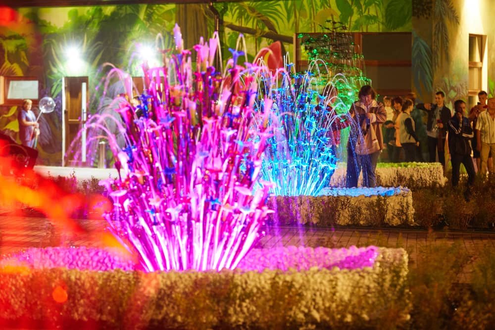 Colorful glass fountain installation with illuminated water jets in public park at night Colorful glass fountain installation with illuminated water jets