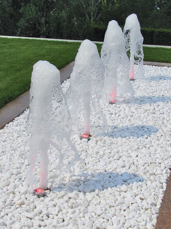 Foamy Ground Jet Fountain Foamy ground water jets on white decorative stones in a landscaped courtyard