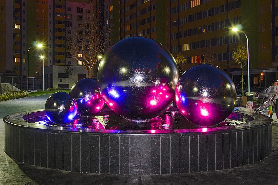 Reflective silver sphere fountain with multiple metal balls placed in a circular granite basin Reflective silver sphere fountain with multiple metal balls