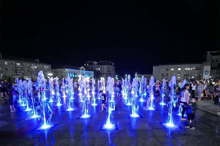 Interactive LED dry deck fountain with dancing water jets and visitors in a public square LED dry deck fountain with interactive jets at night