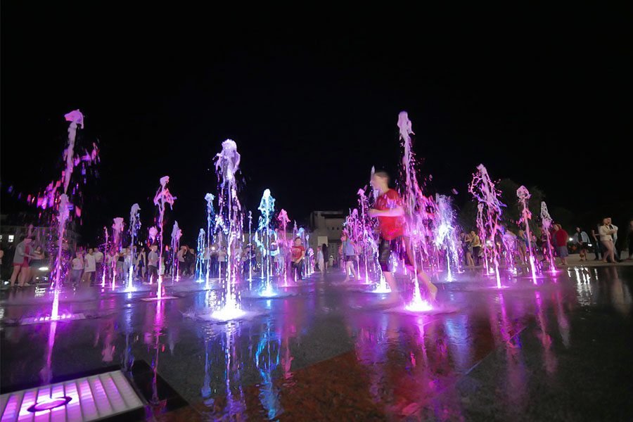 Colorful LED dry deck fountain with interactive dancing jets and children playing at night in a public square Interactive LED dry fountain with children playing at night