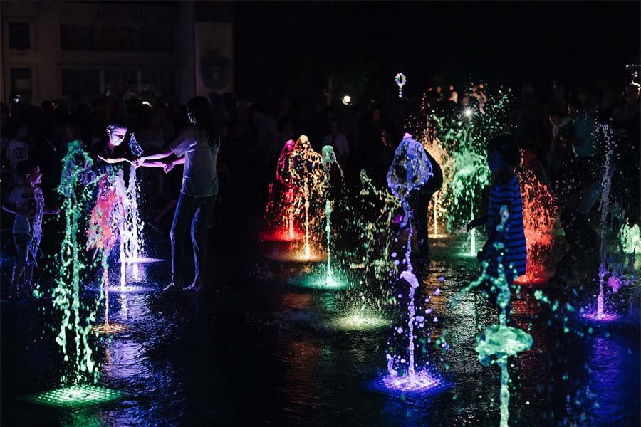 Interactive dry deck fountain with vibrant multicolor LED lighting Colorful LED dry fountain with people interacting at night