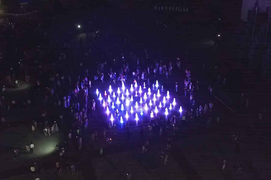 Aerial view of interactive LED dry deck fountain with dancing water jets surrounded by visitors at night Aerial view of LED dry fountain at night