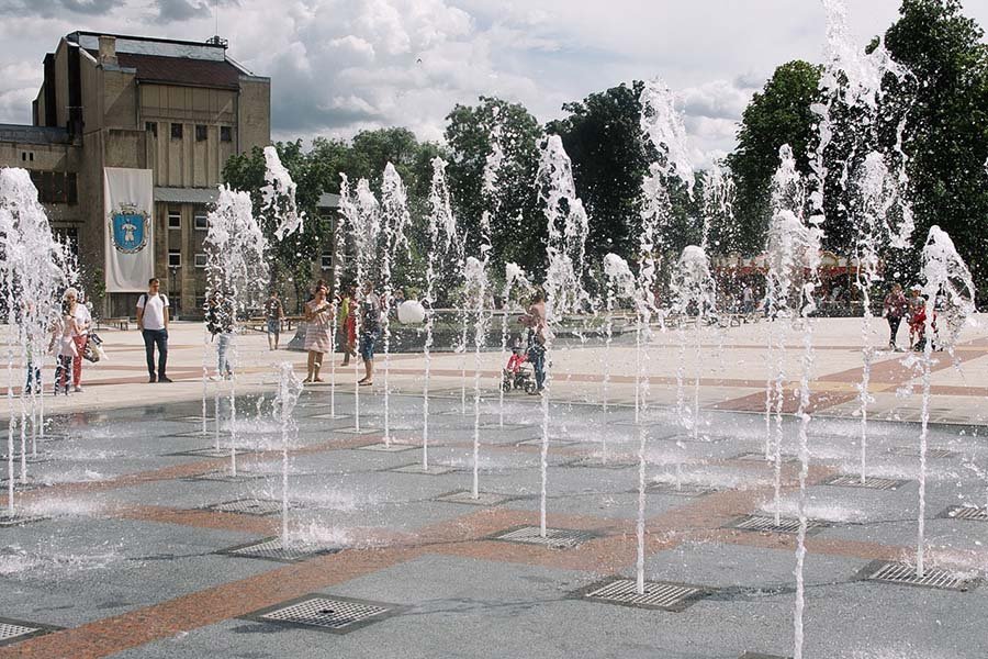 Interactive dry deck fountain with vertical water jets in an urban public square during the day Dry deck fountain with vertical water jets in public square