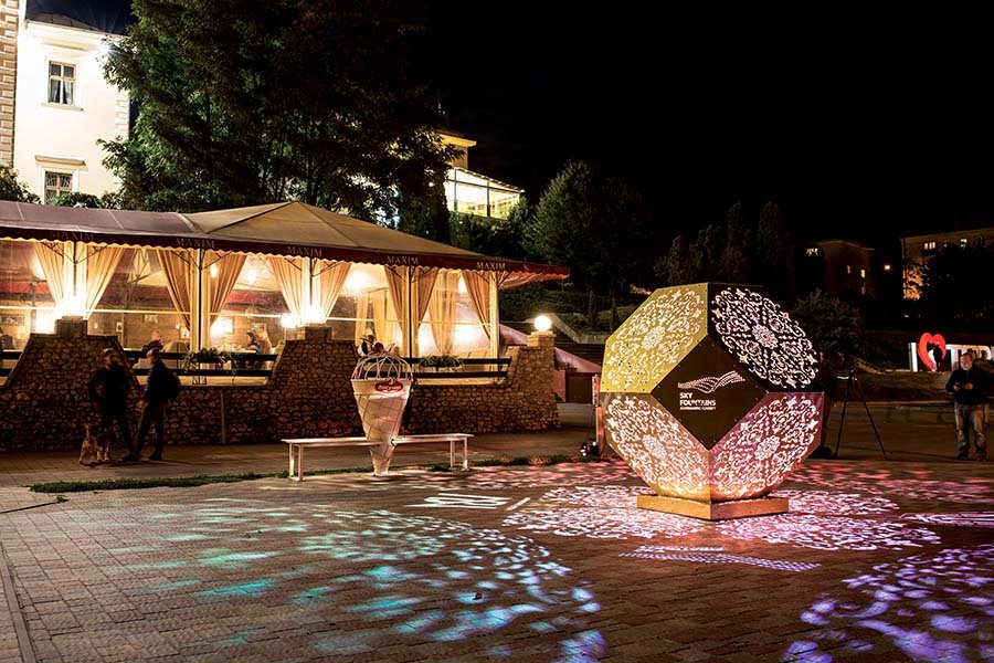 Illuminated geometric sculpture with patterned light projections in a public square Illuminated geometric sculpture with patterned light projections