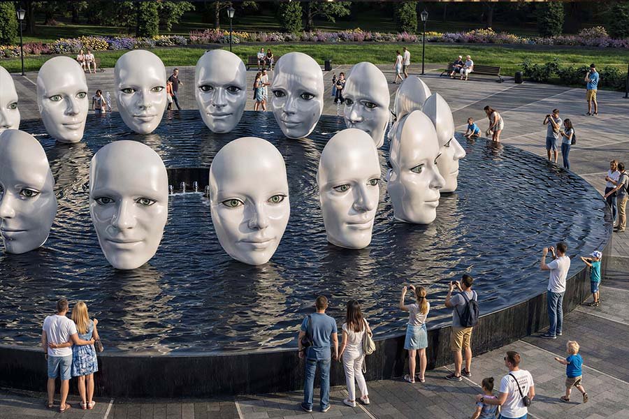 Sculptural fountain installation featuring human face forms in public space Public art fountain with sculptural faces
