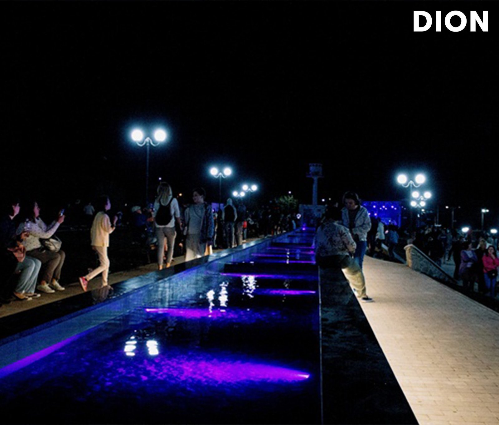 Long LED-lit water channel with purple illumination and visitors walking at night