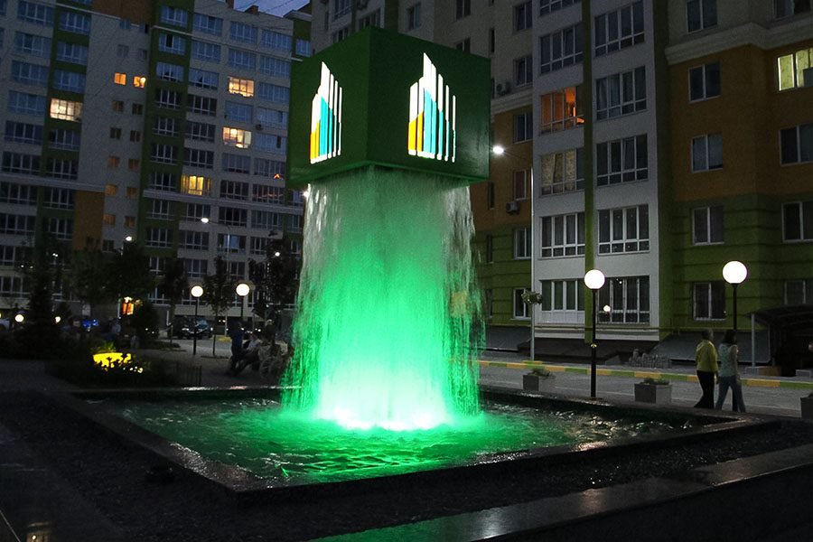 LED-illuminated cube waterfall installation glowing green in a residential courtyard at night