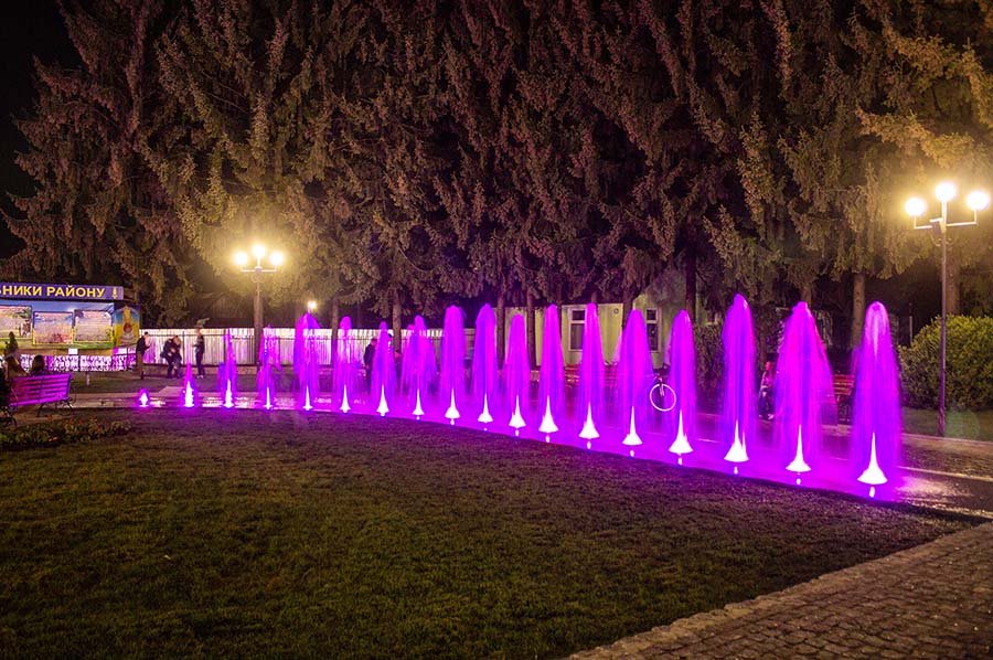 Linear LED fountain jets with purple illumination in a public park at night