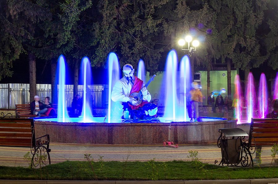 LED fountain with musician sculpture and colorful vertical water jets at night in a public park
