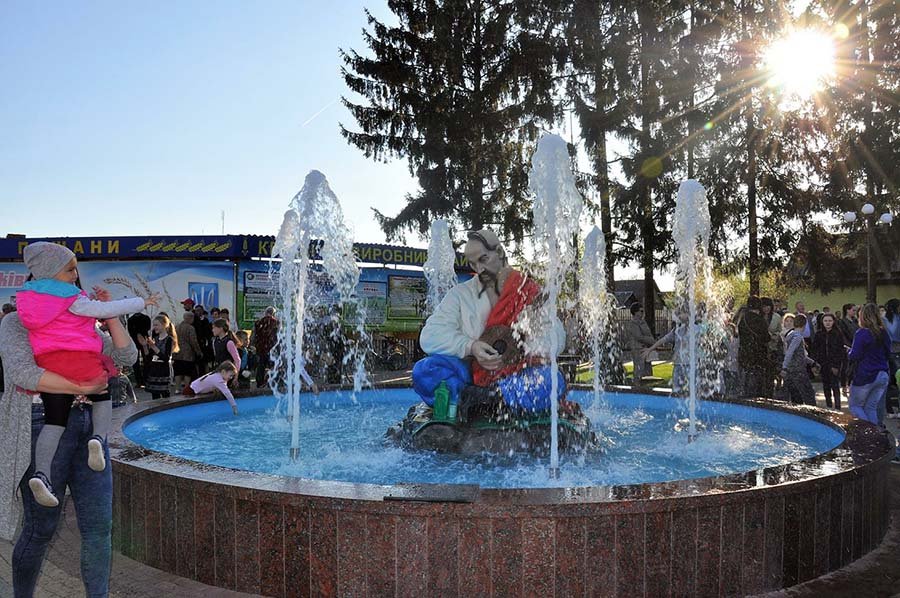 Fountain with musician sculpture and vertical water jets surrounded by visitors in a public park