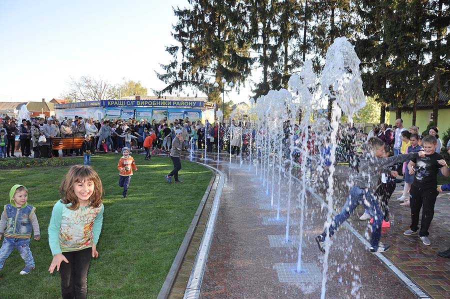 Kids interacting with a row of vertical water jets in a landscaped park area