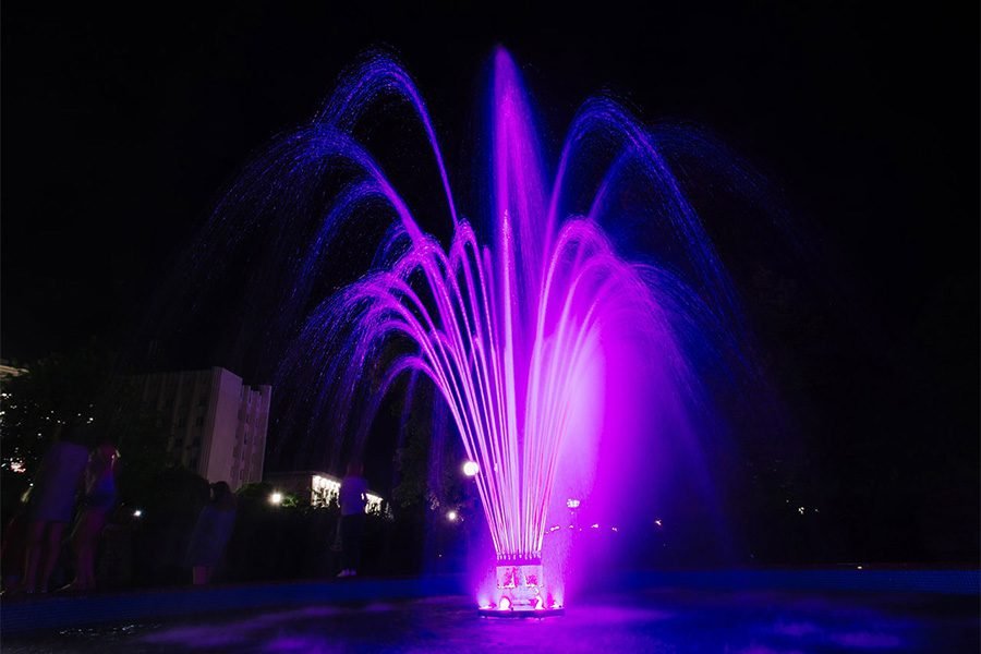 Purple LED fountain with arched water jets at night