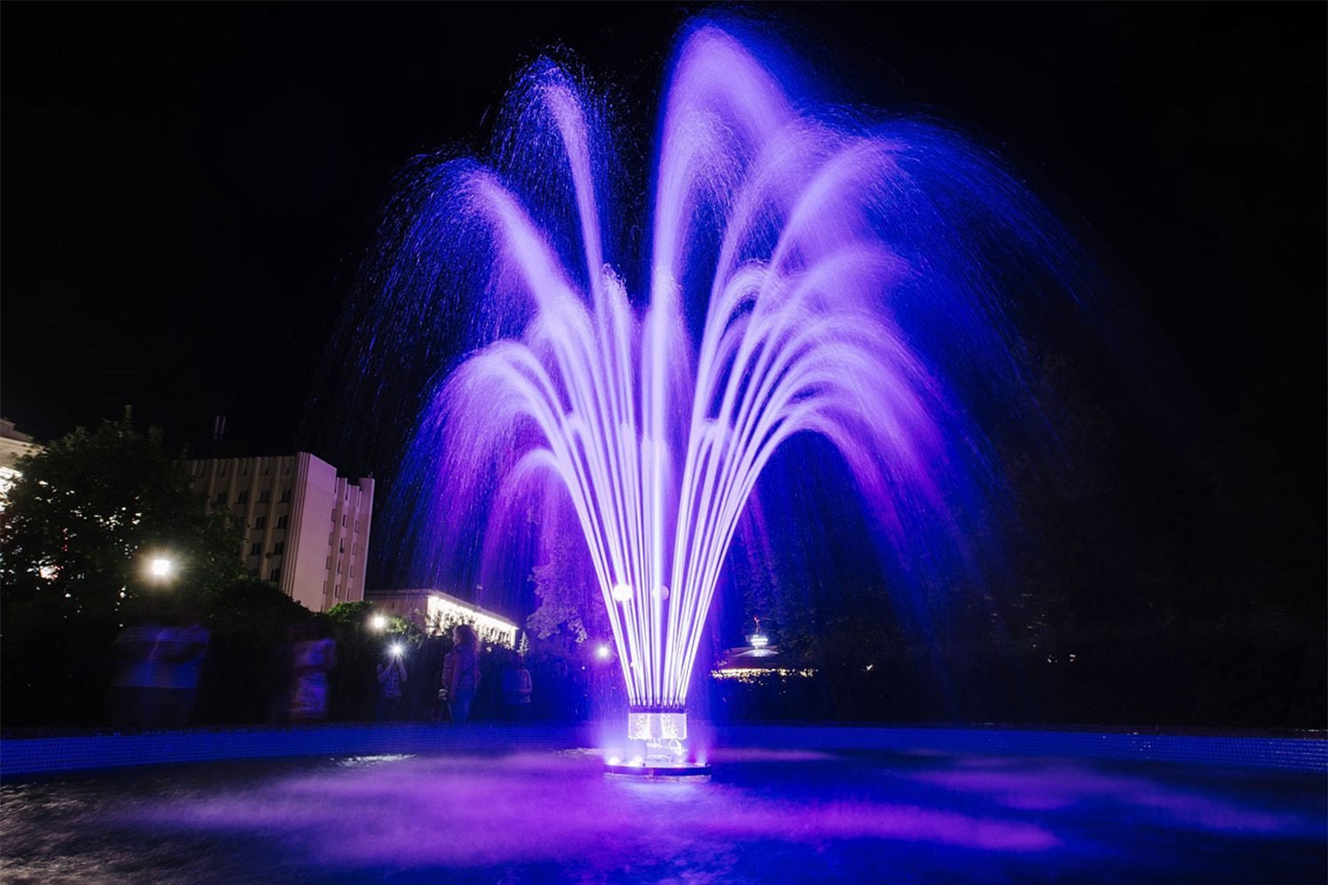 Purple LED fountain with arched water jets at night
