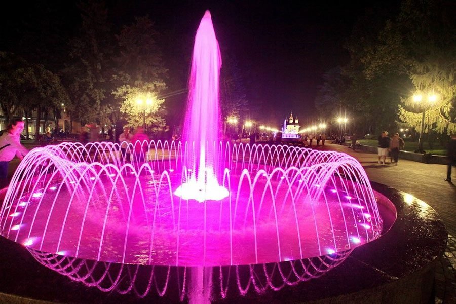 Illuminated decorative fountain with pink LED water jets at night