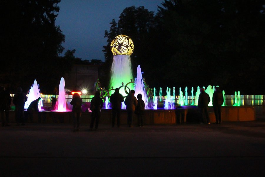 RGB LED fountain with central sculpture and people watching the light show at night