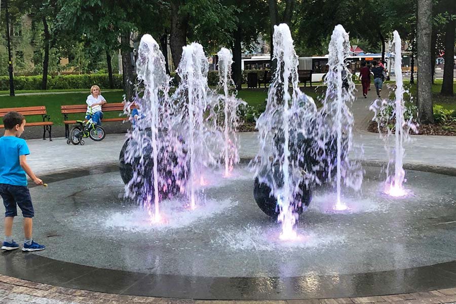 Interactive park fountain with illuminated water jets and sculptural stone spheres