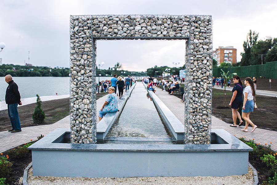 Decorative stone-frame installation over a long shallow water channel on a riverside promenade