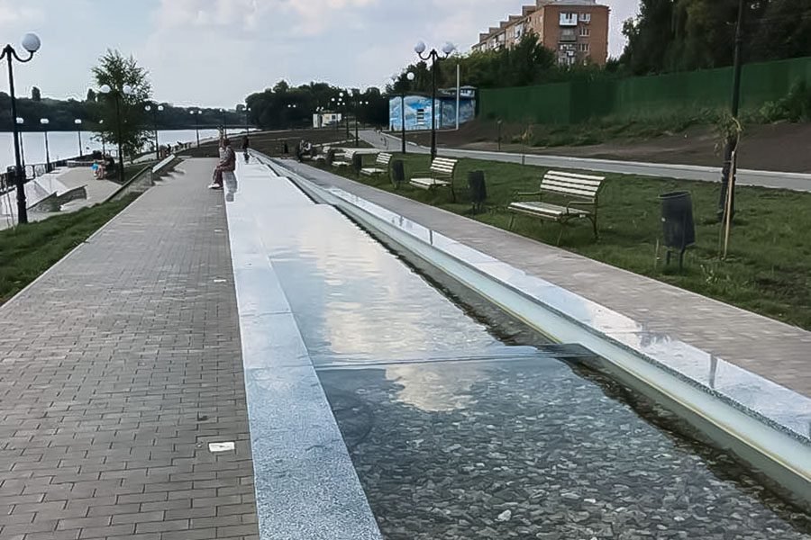 Long shallow water channel cascade along a riverside promenade during the day