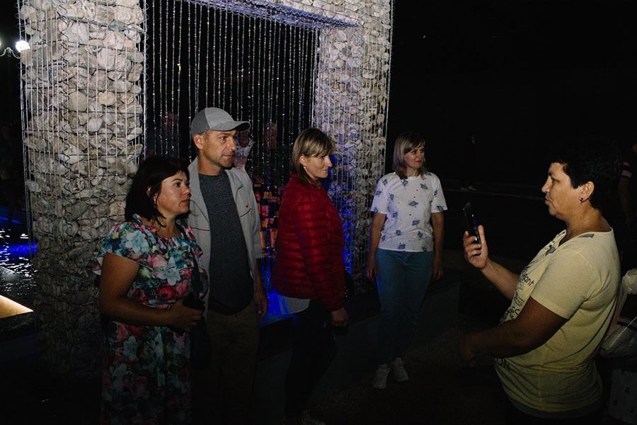 People in front of a stone square arch water feature at night