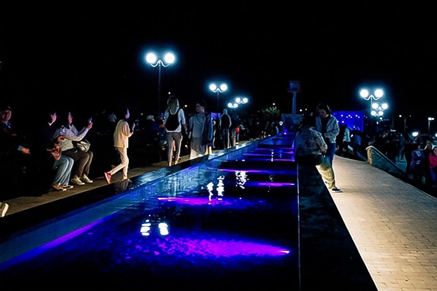 People walking along an LED-lit water channel on a night promenade
