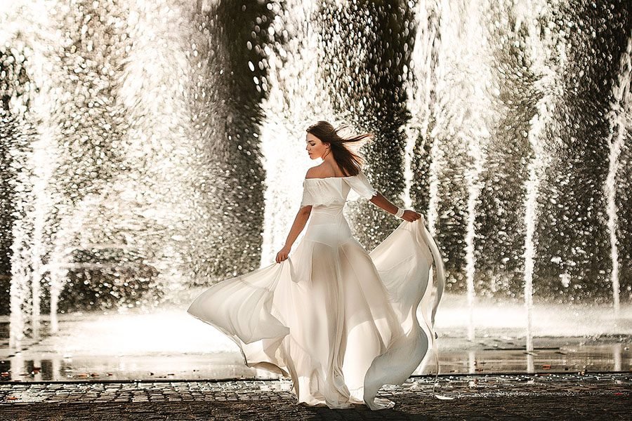 woman in white dress posing by tall fountain jets