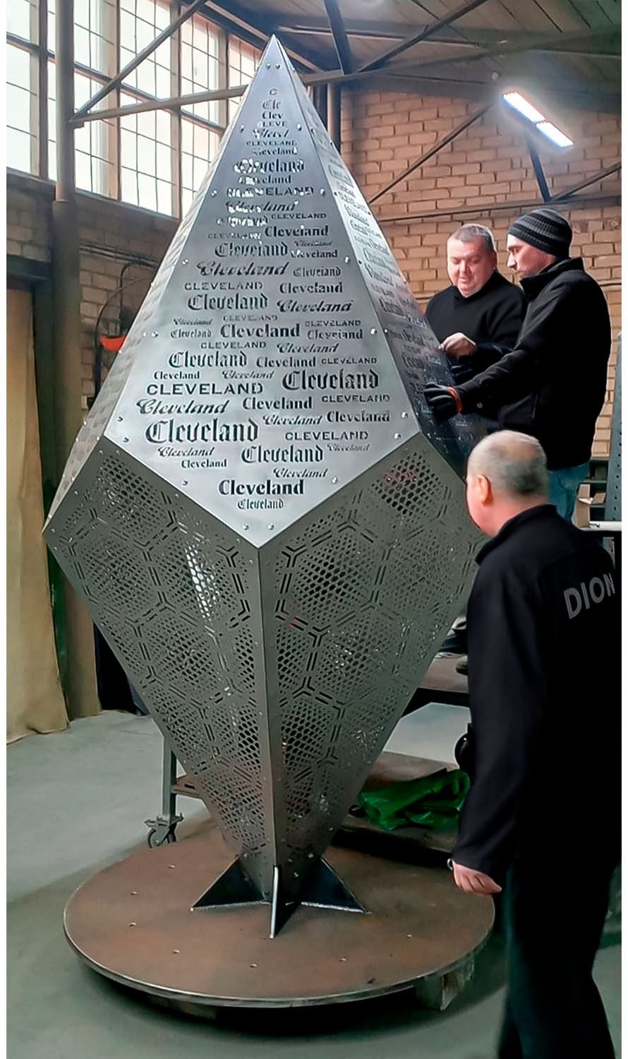 Team DION inspecting and assembling a large perforated metal sculpture with engraved text