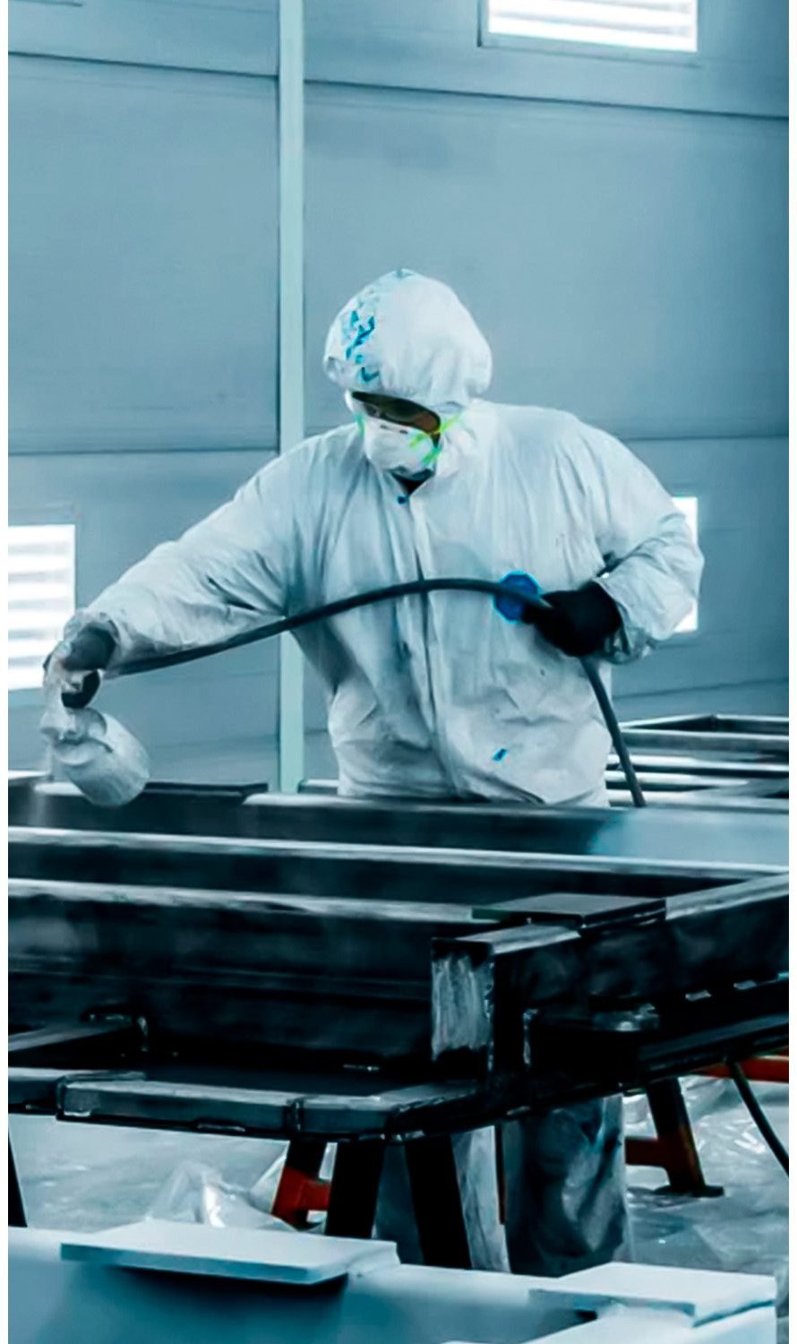 Factory worker DION in protective gear performing surface coating on metal components