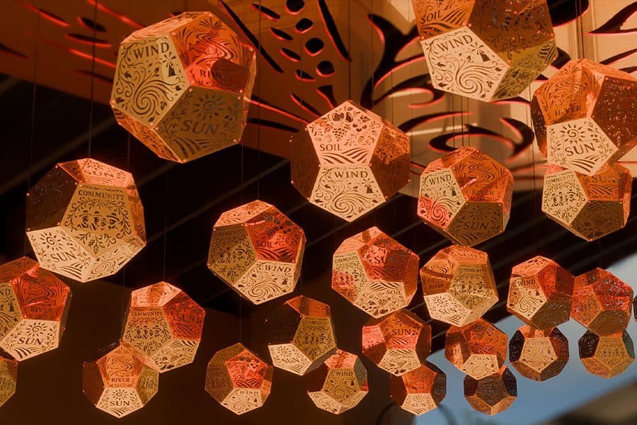 сlose-up view of the installation's Five Elements Kinetic installation at night with gradient lighting golden modules during the day under a canopy